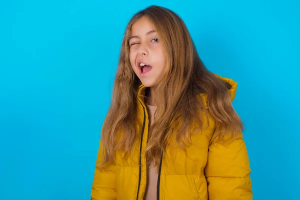 Brunette Kid Girl Wearing Yellow Jacket Blue Background Winking Looking — Stock Photo, Image