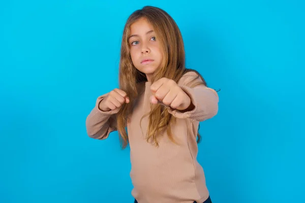 ブルネットの女の子身に着けているセーター上の青の背景パンチ拳で戦うために 積極的かつ怒っている攻撃 脅威と暴力 — ストック写真