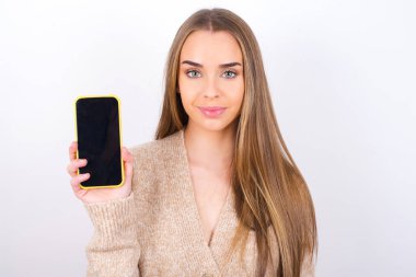 Genç bir kadın kameraya bakıyor ve akıllı telefon ekranı gösteriyor