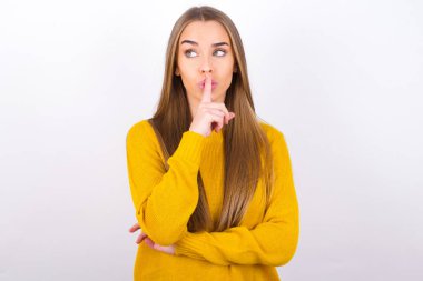 Stüdyoda poz veren genç bir kadın sessiz jest yapıyor