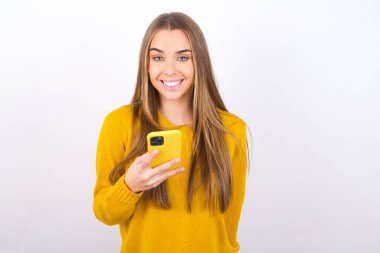 Stüdyoda akıllı telefonla poz veren ve gülümseyen genç bir kadın.