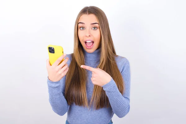 Young Woman Posing Smartphone Studio Pointing Finger — Stockfoto
