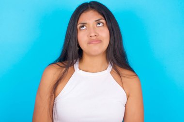 Mavi arka planda beyaz kolsuz bluz giyen genç İspanyol kızın endişeli bir yüzü var. Birbirlerine bakıyorlar, önemli bir şeyi düşünerek üzülüyorlar ve ellerini aşağıda tutuyorlar..
