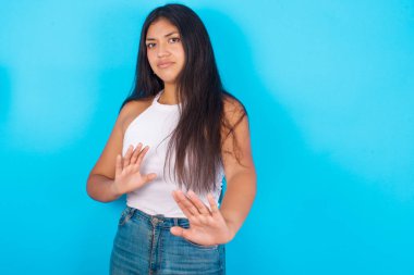 Mavi arka planda beyaz kolsuz bluz giyen ürkek genç bir kız dehşete kapılmış bir ifade takınıyor ve iki eliyle hareket etmeyi bırakıp 