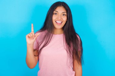 Mavi arka planda pembe tişört giyen hoş görünümlü genç İspanyol kız akıllı bir ifade takınır, bir parmağını kaldırır ve önemli bir şeyi unutmaması gerektiğini hatırlar..