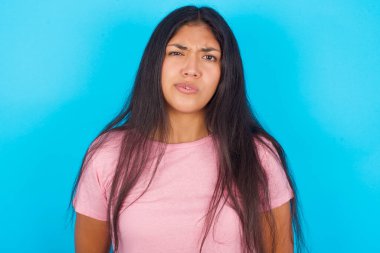 Mavi arka planda pembe tişört giyen genç İspanyol kız tiksinti, isteksizlik, gergin bakışlı, somurtkan suratlı, bir şeyle kızgın görünen..