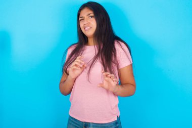 Ne kadar iğrenç! Mavi arka planda pembe tişört giyen hoşnutsuz genç İspanyol kız, iğrenç bir şey gördüğü için tatminsiz yüz ifadesi takındı..