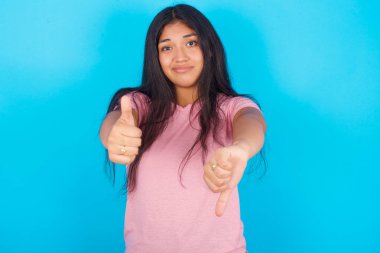 Mavi arka planda pembe tişört giyen İspanyol genç bir kız iyi işaret verdiğinden emin olamıyor. Memnun değil ve etkilenmemiş..