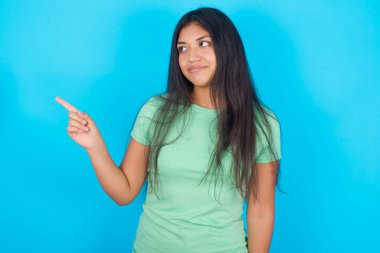 Fotokopi alanında mavi arka plan noktalarının üzerine yeşil tişört giyen İspanyol genç kız en uygun fiyatı öneriyor..