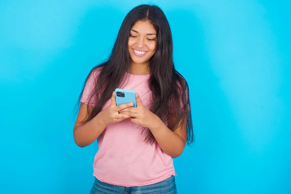 Usmívající Mladá Hispánka Růžovém Tričku Přes Modré Pozadí Pomocí Mobilu — Stock fotografie