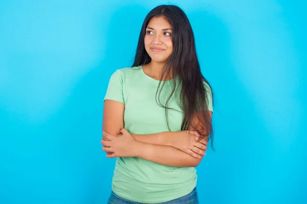 Pleased Young Hispanic Girl Wearing Green Shirt Blue Background Keeps — Fotografia de Stock