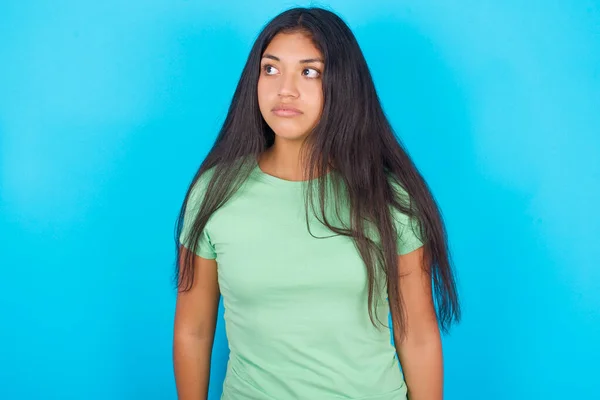 Młoda Latynoska Dziewczyna Zielonym Shircie Niebieskim Tle Spogląda Bok Zdumionym — Zdjęcie stockowe