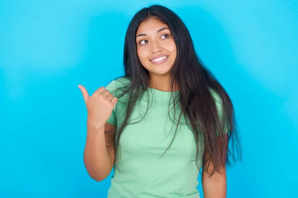 Young Hispanic Girl Wearing Green Shirt Blue Background Points Away — Fotografia de Stock