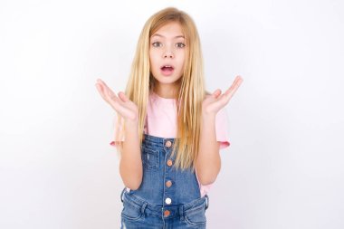 Şaşırmış, korkmuş, beyaz arka planda kot pantolon giyen beyaz bir kız. Belirsizlikle jestler yapıyor, kameraya bakıyor. Şaşırtıcı sorunun cevabını bilmediğinden şaşırıyor.