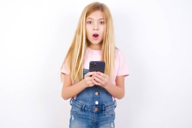 Şok olmuş, beyaz arka planda kot pantolon giyen güzel beyaz bir kız ağzı açık, telefon rehberi reklamları okuyor inanılmaz büyük alışveriş fiyatları var.