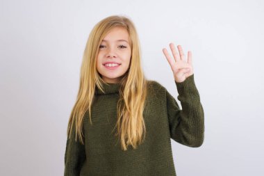 Beyaz arka planda yeşil örülü süveter giyen beyaz çocuk dört numarayı gösterirken kendine güvenen ve mutlu gülümseyen.