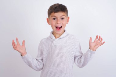 İyimser, beyaz arka plan üzerinde örülü süveter giyen beyaz çocuk sevinçten avuçlarını kaldırıyor, birinden müthiş bir hediye almaktan mutlu, yüksek sesle bağırıyor, heyecanlı manken çığlıkları atıyor..