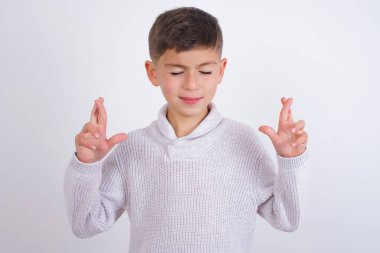 Beyaz arka planda dikilen örgü süveter giyen beyaz çocuk büyük bir umuda sahip, şans diliyor, iyi şansa inanıyor, geniş bir şekilde gülümsüyor. İnsanlar ve dilek kavramı