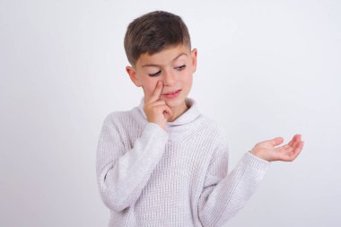 Beyaz arka planda dikilen örgü örülü süveter giyen komik beyaz çocuk elinde yeni bir şey tutuyor. Satın almak istiyorum.!