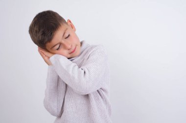 Beyaz arka planda dikilmiş örgü kazak giyen beyaz çocuk yorgun uyur, hayal kurar ve elleri ile birlikte poz verir, gözleri kapalı gülümserdi..