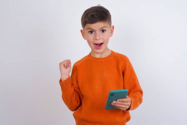 Beyaz arka planda dikilmiş örgü turuncu süveter giyen beyaz çocuk portresi.