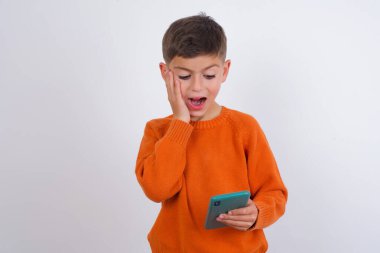 Kafkas çocuk örgü turuncu süveter giyiyor beyaz arka planda duruyor hücresinde yeni uygulamayla SMS okuyor.