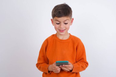 Kafkas çocuk örgü turuncu süveter giyiyor beyaz arka planda cep telefonu sohbetini boş vakitlerinde yapıyor. .