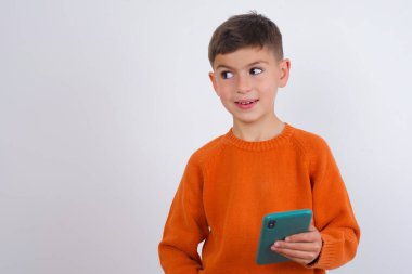 Beyaz arka planda dikilen örgü turuncu süveter giyen beyaz çocuk yeni bir hücre gösteriyor.