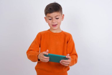 Beyaz arka plan üzerinde örülmüş turuncu süveter giyen beyaz çocuk hücrede el ele tutuşmuş video oyunları oynuyor ya da sohbet ediyor.