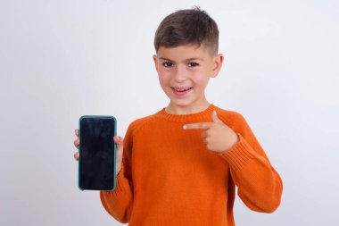 Çekici, neşeli, beyaz arka plan üzerinde örülmüş turuncu süveter giyen beyaz çocuk.