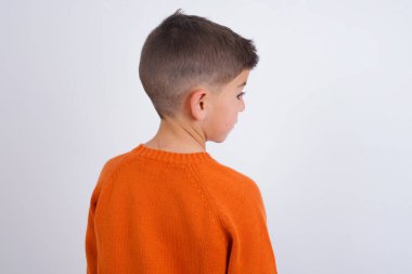 Beyaz arka plan stüdyosunun üzerinde örgü örülmüş turuncu süveter giyen beyaz bir çocuğun arka plan görüntüsü..