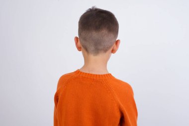 Beyaz arka planda dikilen örgü turuncu süveter giyen beyaz bir çocuğun arka görüntüsü. Stüdyo Çekimi.