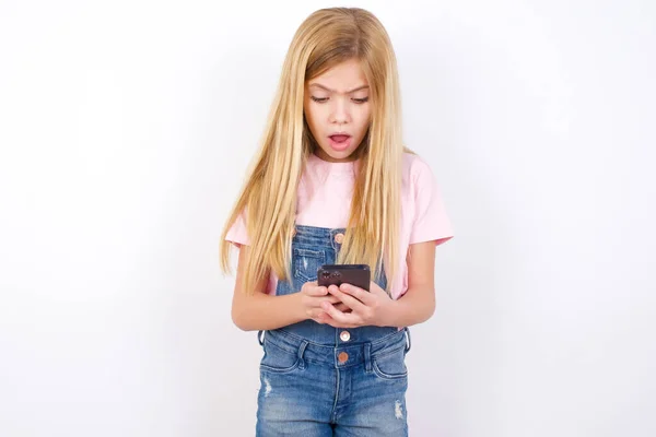 白い背景の上にデニムジーンズを身に着けている焦点を当てた美しい白人の女の子は ソーシャルメディアのニュースを読んでスマートフォンを使用するか または重要な電子メール — ストック写真
