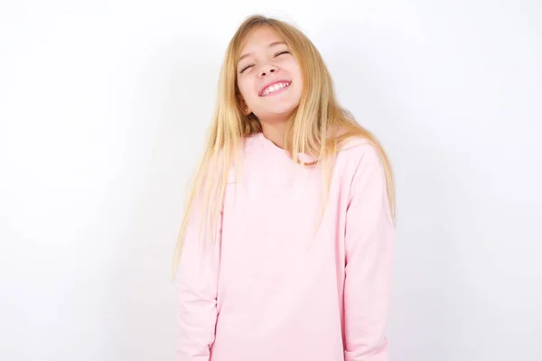积极漂亮的高加索小女孩 身穿粉色毛衣 背景洁白 满脸喜色 闭上双眼 笑着露出洁白完美的牙齿 — 图库照片
