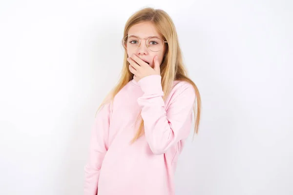 白地にピンク色のセーターを着た美しい白人の少女が口を覆いカメラを見て不思議そうな噂を信じられない — ストック写真