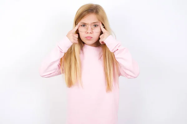 认真集中的 漂亮的 穿着粉色毛衣 背景为白色的高加索小女孩 总是把手指放在太阳穴上 试图缓和紧张 用思想集中起来 并记住重要的考试信息 — 图库照片