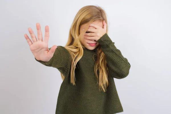 白い背景に緑色のニットセーターを着て白人の子供の女の子は目を覆い 手のひらで目を覆い ジェスチャーを止め 皆から非表示にしようとします — ストック写真