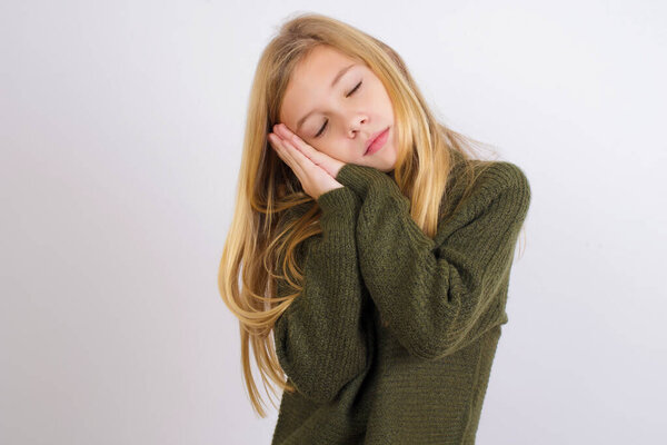 Caucasian kid girl wearing green knitted sweater against white background sleeping tired dreaming and posing with hands together while smiling with closed eyes.