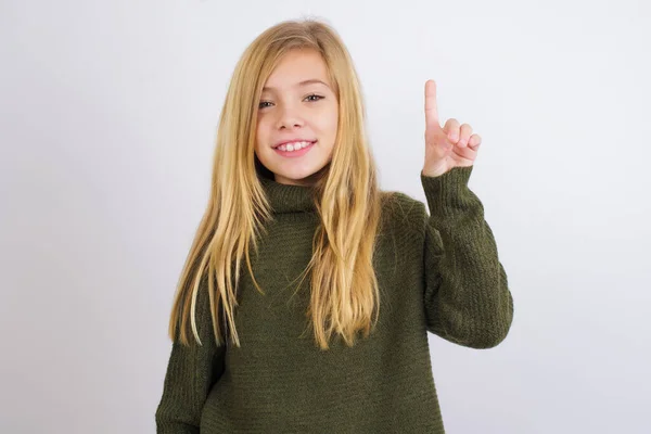 白地に緑色のニットセーターを身に着けている白人の子供の女の子が表示され 指の数1で指摘しながら 自信と幸せ — ストック写真
