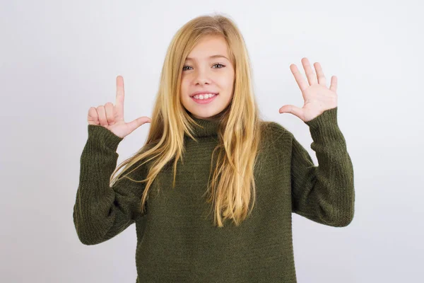 白人の子供の女の子身に着けています緑のニットセーターに白い背景に表示され 指番号7で指摘しながら 自信と幸せ — ストック写真
