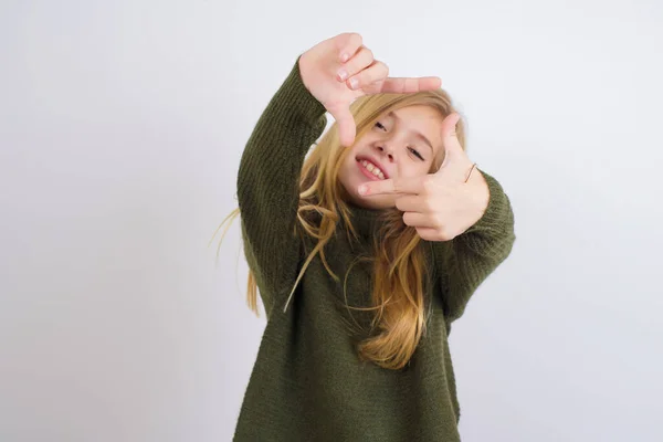 白地に緑色のニットセーターを着て手で指のフレームを作る白人の子供の女の子 創造性と写真の概念 — ストック写真
