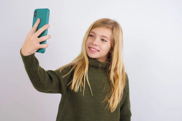 白人の子供の女の子身に着けています緑のニットセーターに白の背景笑顔と取りますA自己撮り準備にそれを投稿する彼女のソーシャルメディア — ストック写真