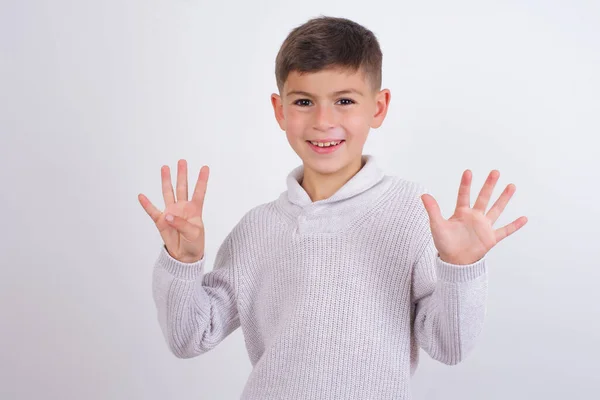 Beyaz arka planda duran örgü süveter giyen beyaz çocuk dokuz numaralı parmaklarını göstererek gülümsüyor ve mutlu..