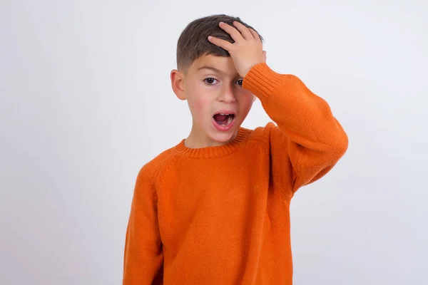 白人の少年は 誤って頭の上に手で驚いて白い背景に立ってニットオレンジのセーターを着て エラーを覚えている 忘れられた悪い記憶の概念 — ストック写真