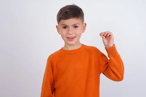 Белый Мальчик Вязаном Оранжевом Свитере Стоящем Белом Фоне Показывая Рукой — стоковое фото