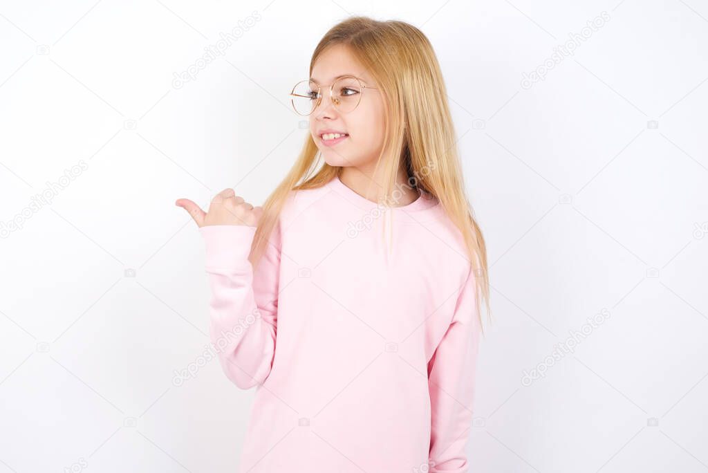 beautiful caucasian little girl wearing pink sweater against white background points away and gives advice demonstrates advertisement