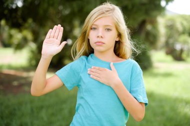 Mavi tişörtlü beyaz bir kız çocuğu göğsü ve avucu açık küfür ediyor ve sadakat yemini ediyor.