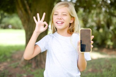 Beyaz tişörtlü küçük beyaz kız dışarıda duruyor. Hücrede el ele tutuşup 