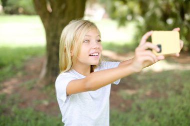 Beyaz tişörtlü beyaz bir kız çocuğu sosyal medyada yayınlamak için selfie çekiyor ya da arkadaşlarıyla görüntülü görüşme yapıyor..