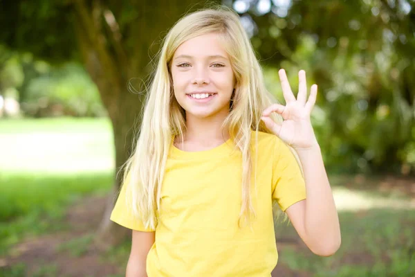 美しい白人の小さな子供の女の子身に着けている黄色のTシャツ立って屋外ホールド手腕キーシンボルおもちゃアドバイス新規性のニュース — ストック写真
